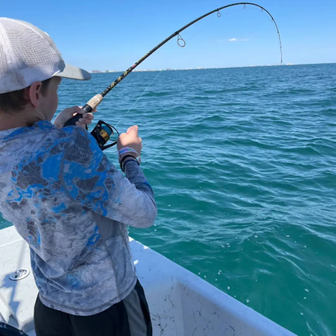 A young fisherman fighting a fish he's reeling in on an orange beach fishing charter with Navigator Charters.